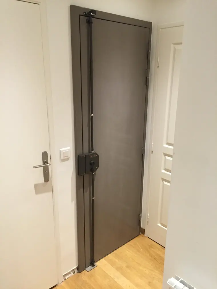 Porte blindée gris taupe et sa serrure en applique, posée dans l'entrée d'un appartement