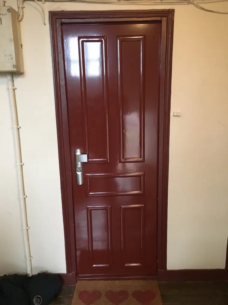 Porte blindée bordeaux à panneaux moulurés, posée sur un palier d'immeuble ancien