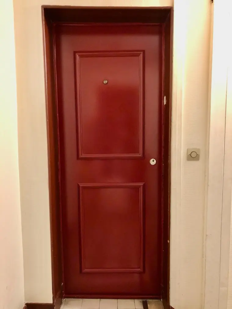 Porte blindée bordeaux à deux panneaux moulurés, vue depuis le palier