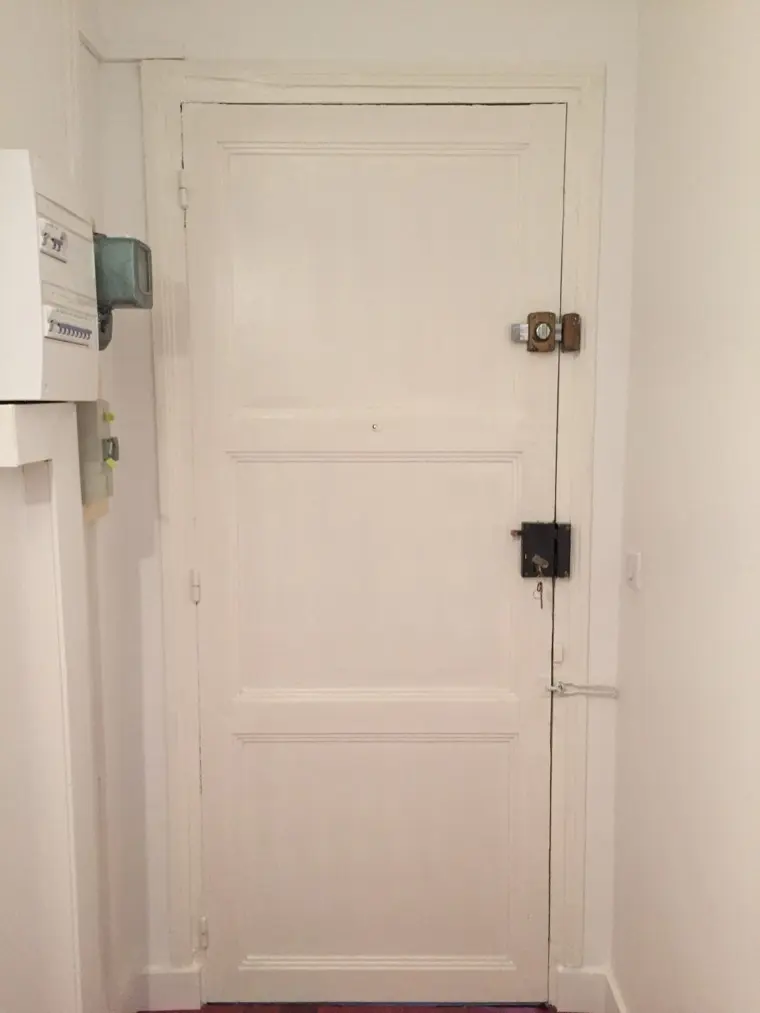 Porte d'appartement ancienne équipée de deux serrures en applique, clé engagée dans la serrure basse