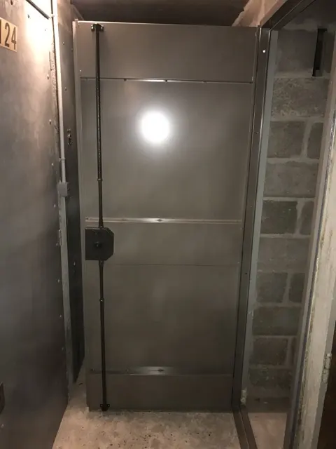 Porte de cave en acier équipée d'une serrure en applique, dans un sous-sol en parpaings