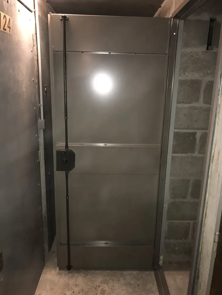 Porte de cave en acier équipée d'une serrure en applique, dans un sous-sol en parpaings