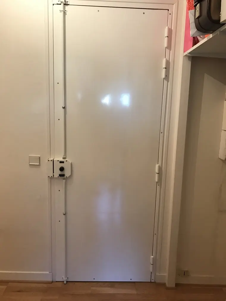 Serrure multipoints en applique posée sur une porte blanche, tringles haute et basse apparentes