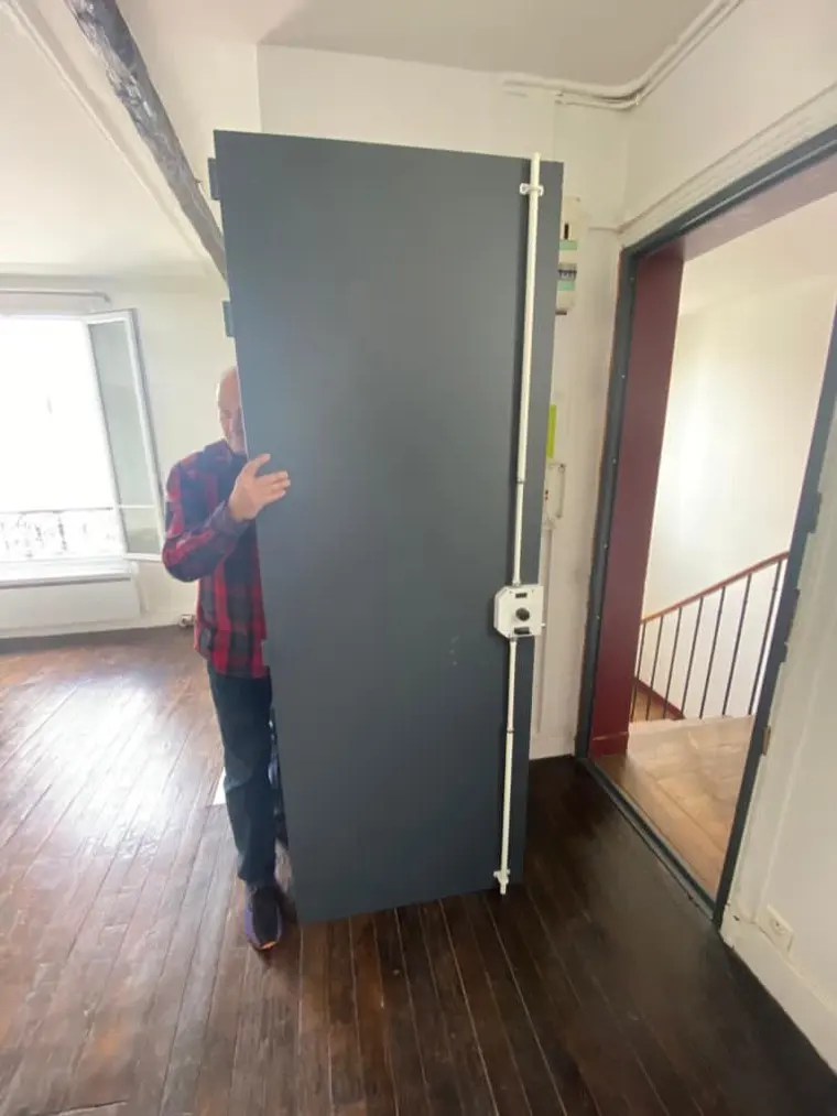 Serrurier présentant un vantail blindé gris ardoise pendant la pose, tringle de verrouillage visible