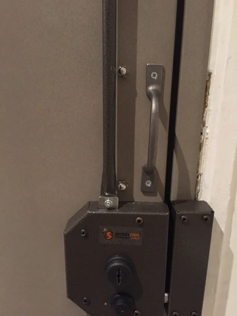 Serrure Securystar en applique posée sur une porte blindée, tringle et coffre visibles
